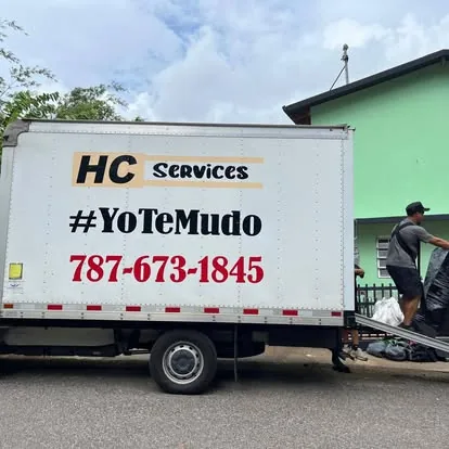 Camión de HC Services rotulado con #YoTeMudo y el teléfono, mientras el equipo carga una mudanza